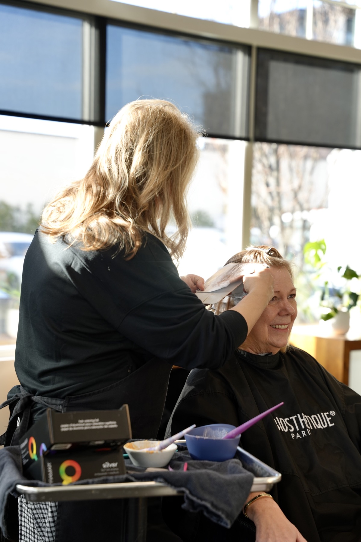 Best Kelowna Hair Salon: Stylist applying hair colour for a smiling client